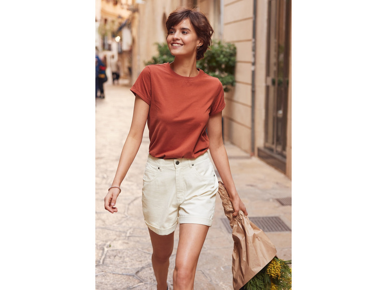 Eine Frau in einem orangen T-Shirt und weißen Shorts geht die Straße entlang.