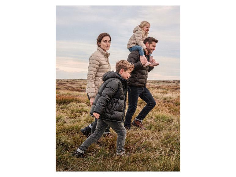 Familie in warmen Jacken und robusten Schuhen spaziert durch eine Graslandschaft.