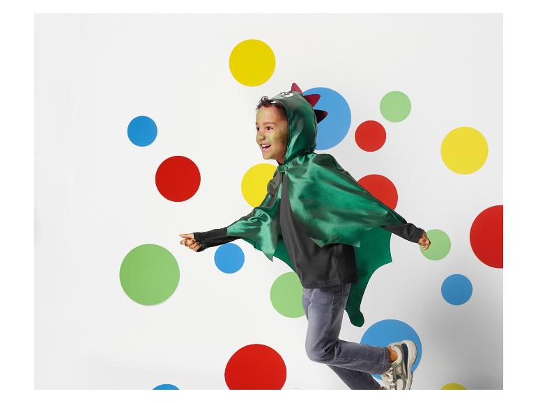 Ein Kind trägt einen grünen Drachenumhang und rennt durch einen Raum mit bunten Punkten.