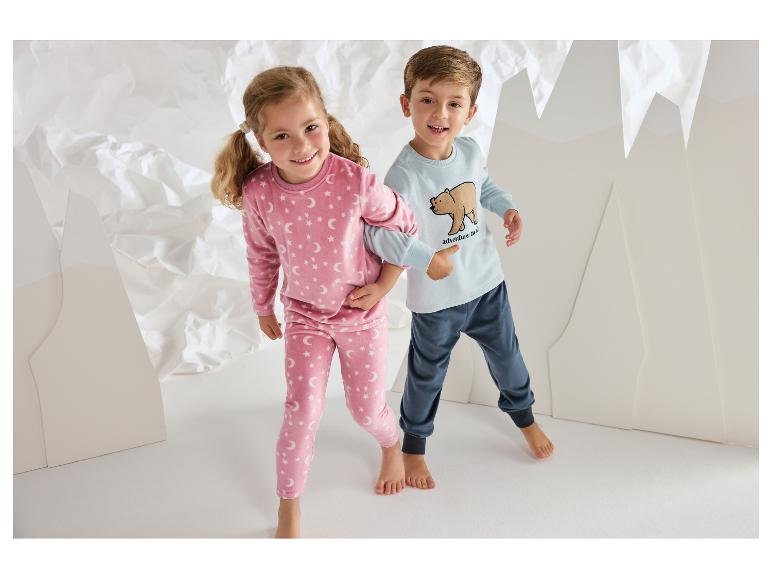 Lächelnde Kinder in gemütlichen Pyjamas mit Sternen- und Bärenmustern.