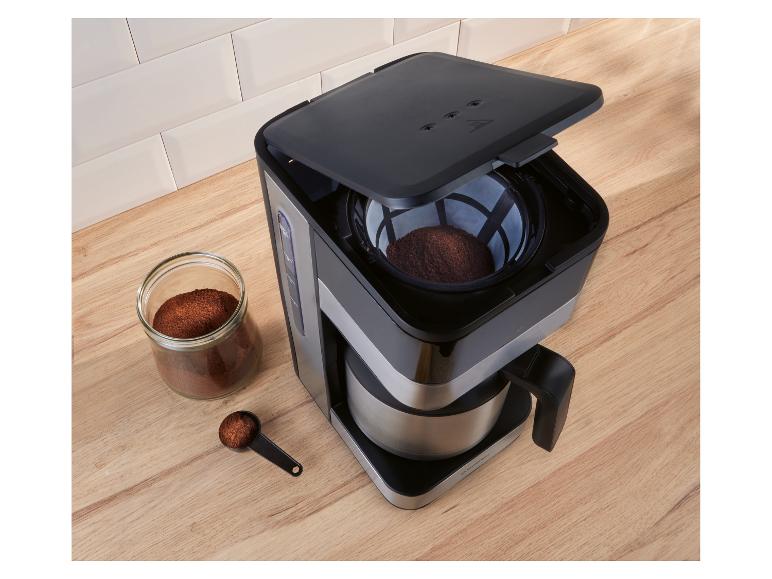 Filterkaffeemaschine mit gemahlenem Kaffee in einem Glas und Messlöffel auf einer Holztheke.