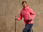 Eine Frau in einer rosa McKinley Jacke und blauen Hosen mit Wanderstöcken.