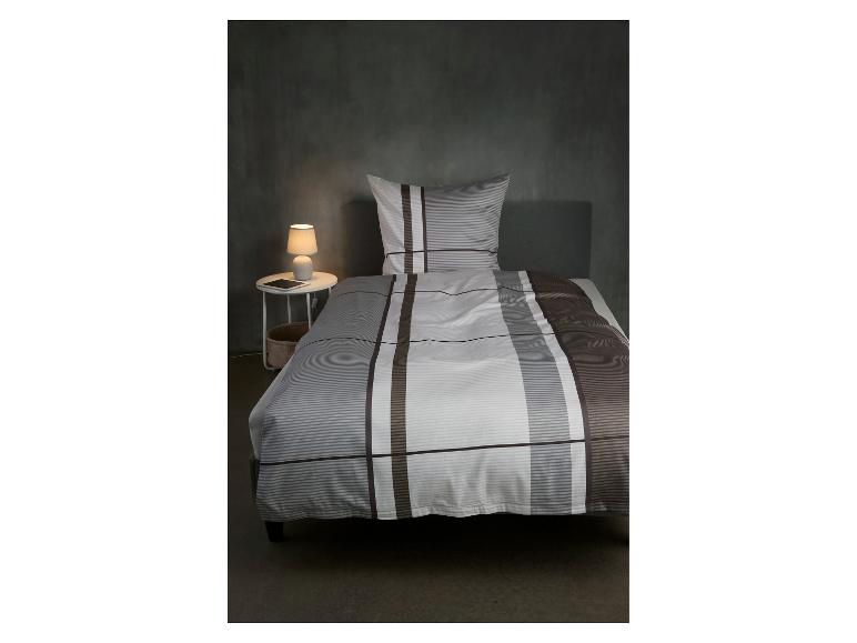 Schlafzimmer mit gestreifter Bettwäsche, Nachttisch und Lampe.