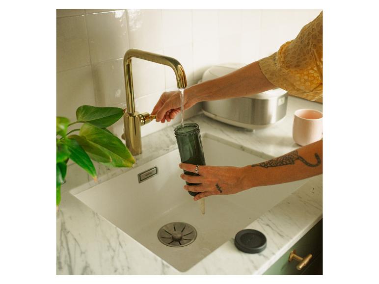 Hand füllt dunkle Flasche mit Wasser aus Küchenhahn.