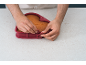 Hände lösen eine herzförmige Silikon-Backform mit einem gebackenen Kuchen.