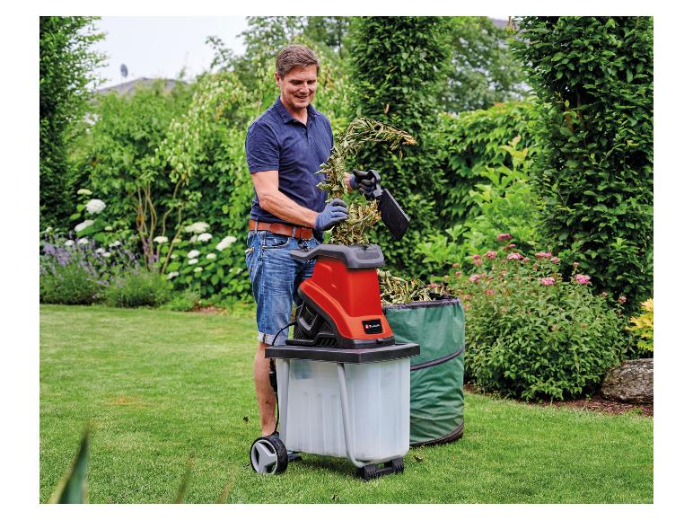 Mann zerkleinert Gartenabfälle mit einem roten Gartenhäcksler in einem grünen Garten.