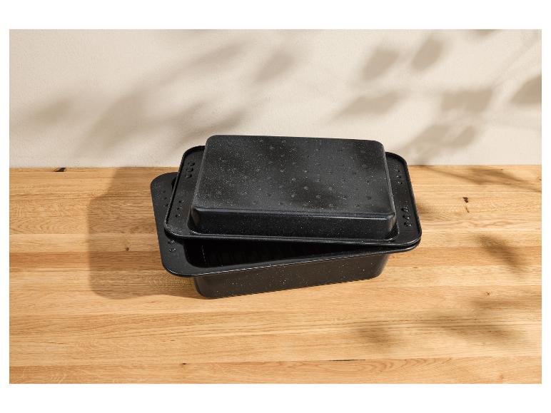 Zwei schwarze rechteckige Bräter mit gesprenkelter Oberfläche auf einem Holztisch.
