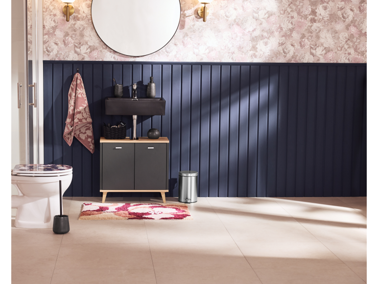 Badezimmer mit schwarzem Waschtisch, Toilette, floralem Teppich und marineblauer Paneelwand.