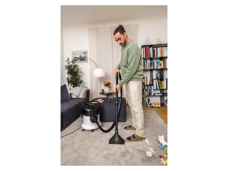 Mann reinigt Teppich mit Nasssauger im Wohnzimmer.