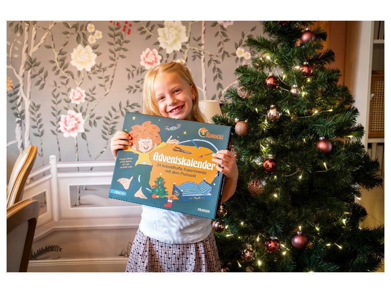 Mädchen hält einen FRANZIS Adventskalender für Kinder vor dem Weihnachtsbaum.