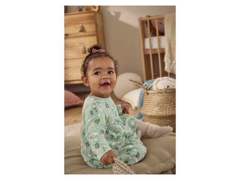 Glückliches Baby in einem Blumenkleid sitzt auf einem Kissen im Kinderzimmer.