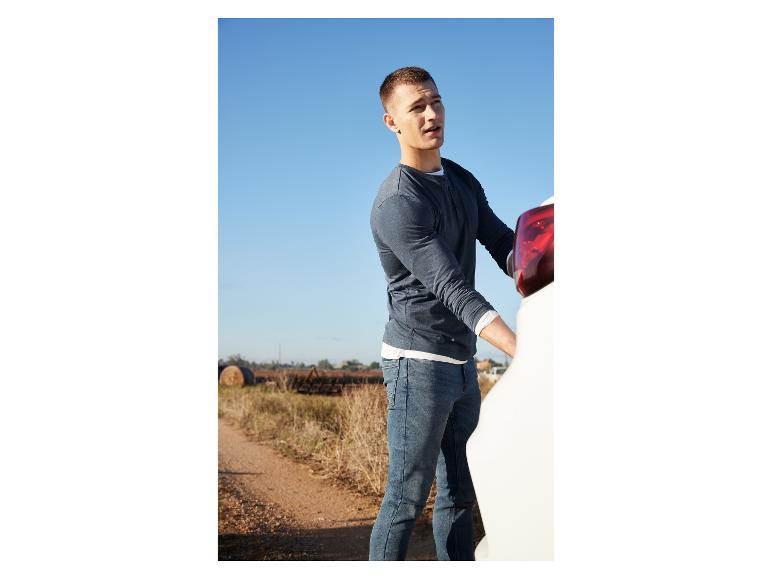 Ein Mann in einem blauen Pullover und Jeans steht neben einem weißen Auto.