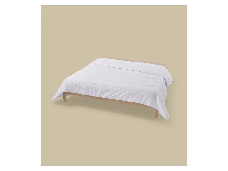 Eine weiße Bettdecke auf einem hellen Holzlattenrost vor beigem Hintergrund.