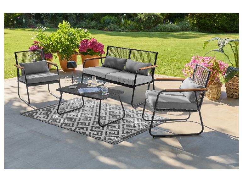Gartenmöbel-Set mit Sofa, zwei Sesseln, Couchtisch und Teppich auf einer Terrasse.