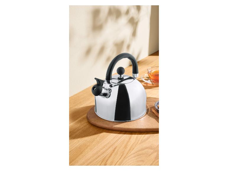 Glänzender Teekessel aus Metall mit schwarzem Griff auf einem Holztisch mit einer Tasse Tee.