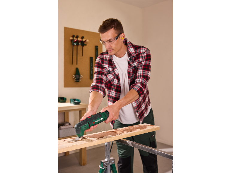 Mann benutzt ein Multifunktionswerkzeug zum Schaben von Holz, trägt Schutzbrille und Gehörschutz.