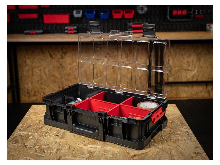 Offener Werkzeugkasten mit transparentem Deckel und roten Fächern auf einer Holzwerkbank.