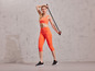Frau in orangefarbenem Sport-BH und Leggings mit einem Widerstandband.