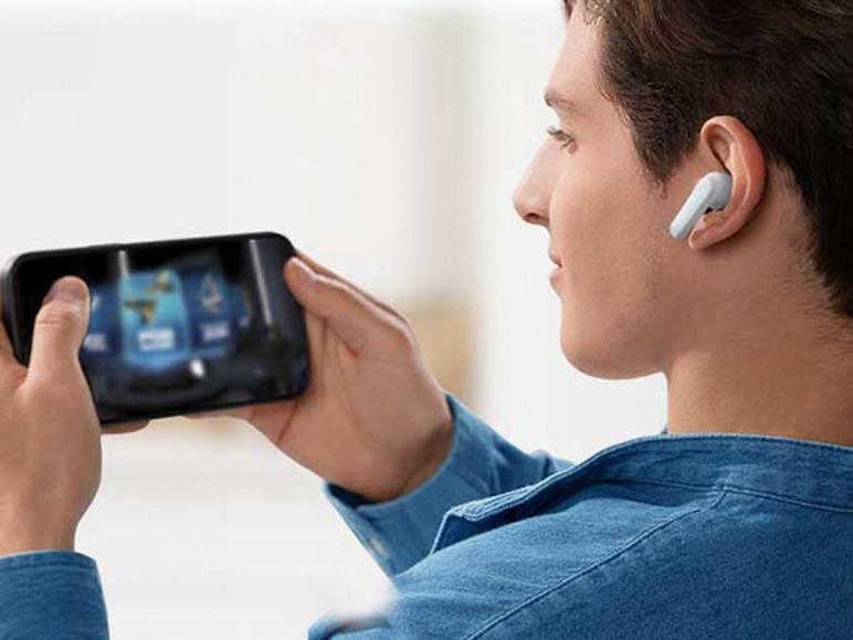 Mann in Jeanshemd spielt auf Smartphone, trägt einen weißen In-Ear-Kopfhörer.