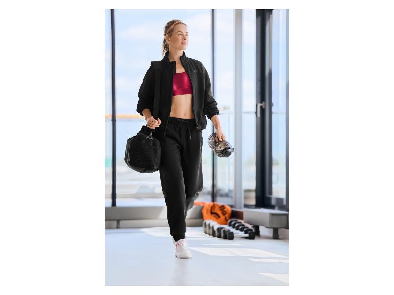 Frau in CRIVIT Sportjacke mit Sporttasche und Trinkflasche.