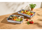Zwei Backbleche mit geröstetem Gemüse und Mais auf einem Holztisch.