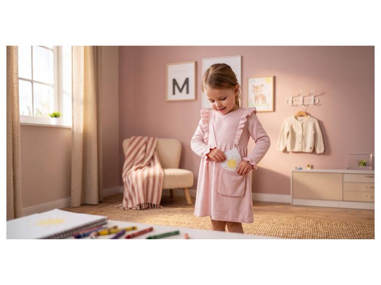 Mädchen in rosa Kleid steckt Sonnenzeichnung in Tasche, im Kinderzimmer.