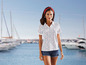 Frau trägt ein weißes Poloshirt mit Anker-Print und Jeans-Shorts, im Hintergrund sichtbare Yachten.