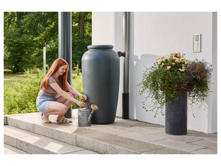 Frau füllt Gießkanne aus einer Regentonne im Garten.
