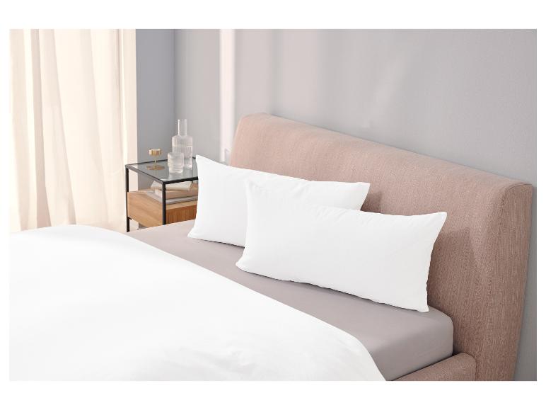 Weiße Bettwäsche und Kissen auf einem Bett mit hellrosa Kopfteil.