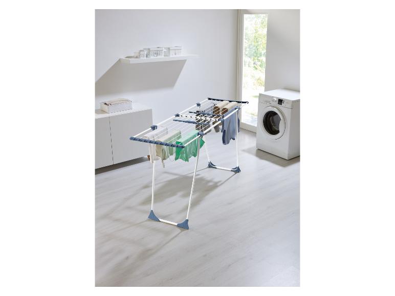Wäscheständer mit Kleidung in einem Waschraum mit Waschmaschine und Schränken.