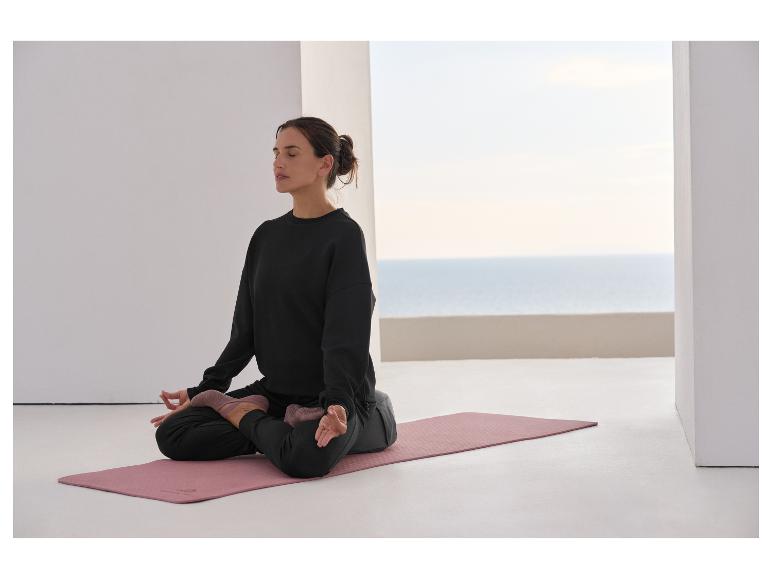 Frau meditiert auf einer Yogamatte, trägt schwarzes Sweatshirt und Hose.