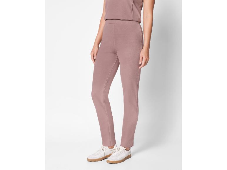 Eine Frau trägt eine rosa Hose und weiße Sneaker.