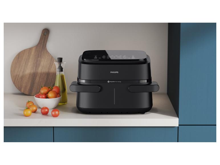 Eine schwarze Philips Heißluftfritteuse auf einer Küchenarbeitsplatte mit Tomaten und Olivenöl.