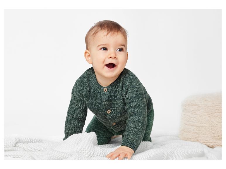 Ein entzückendes Baby in einem grünen Strickoverall.