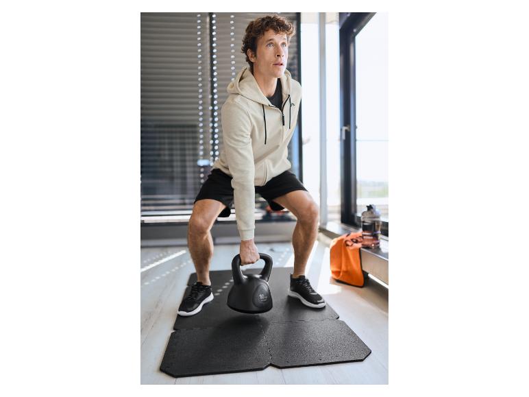 Mann in Kapuzenpullover und Shorts, der eine 10 kg Kettlebell auf einer Bodenmatte hebt.