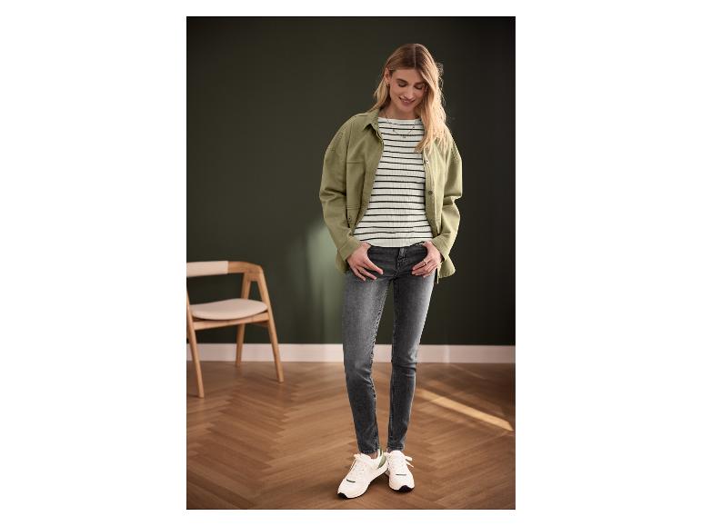 Frau trägt grüne Jacke, gestreiftes Oberteil, graue Jeans und weiße Sneaker.