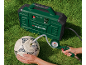 Grüner Kompressor bläst einen weißen Fußball auf Gras auf, eine Person hält den Ball und das Manometer.