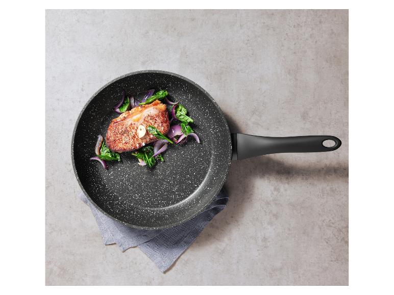 Bratpfanne mit gekochtem Fleisch, Spinat und roten Zwiebeln auf grauem Hintergrund.