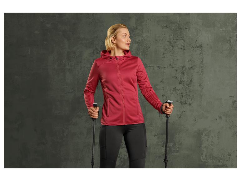 Frau in roter Jacke und schwarzen Hosen mit Wanderstöcken.