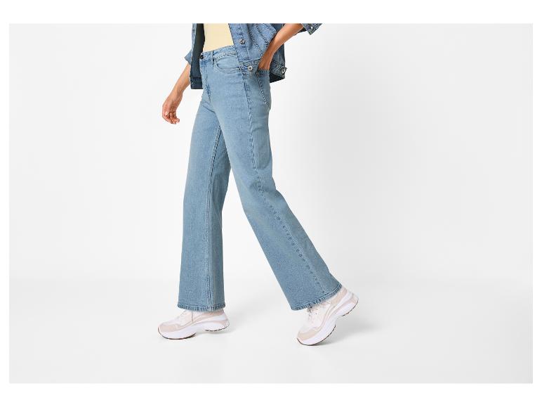 Person in hellblauen Jeans, gelbem Top und Jeansjacke, mit weißen Sneakern.