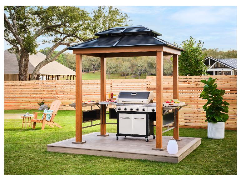 Grillpavillon mit Grill, Gartenmöbeln und Pflanzen in einem Garten.