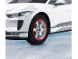 Weißes Elektroauto mit roten Textil-Schneeketten auf Schnee.