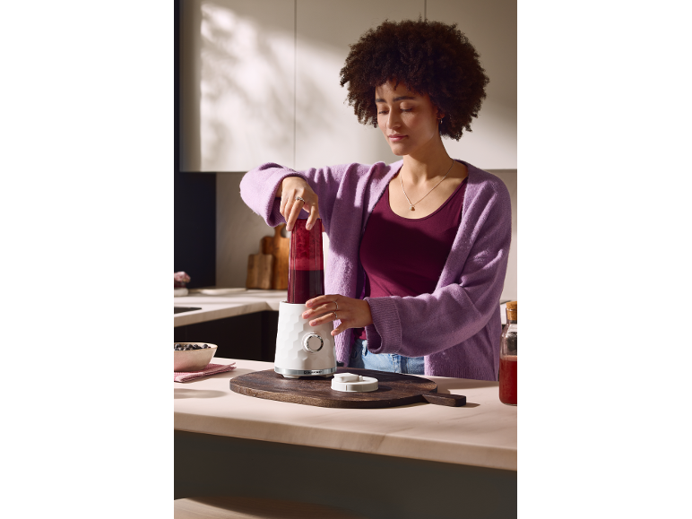 Eine Frau bereitet in der Küche einen Smoothie mit einem Standmixer zu.