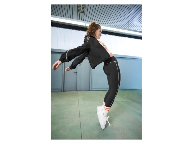Frau in schwarzer Sportjacke und Leggings, mit weißen Socken und Schuhen, tanzend.