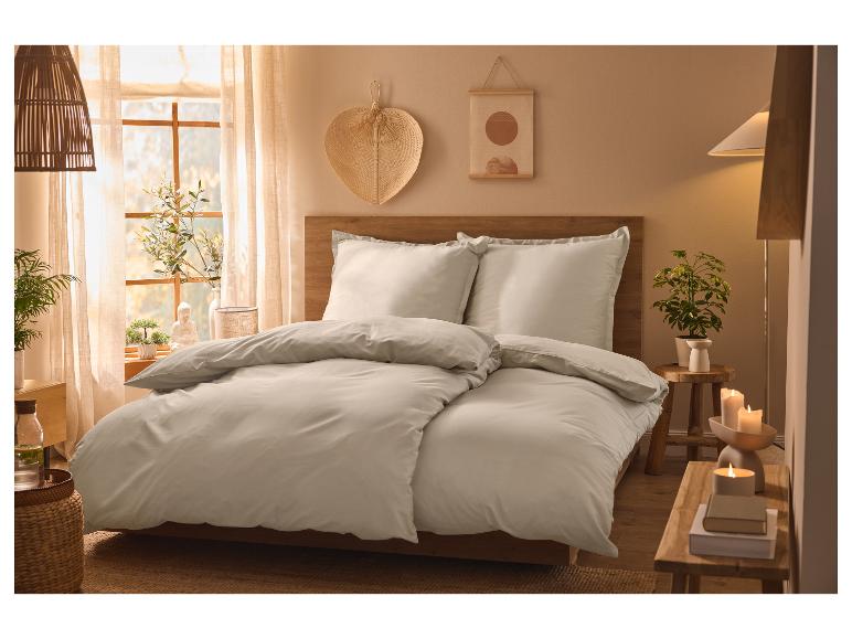 Hellgraues Bettwäsche-Set auf einem Holzbett in einem gemütlichen Schlafzimmer.