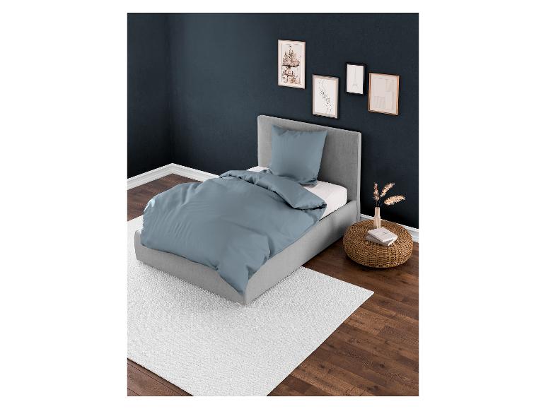 Ein graues Bett mit einer blauen Decke und einem weißen Teppich