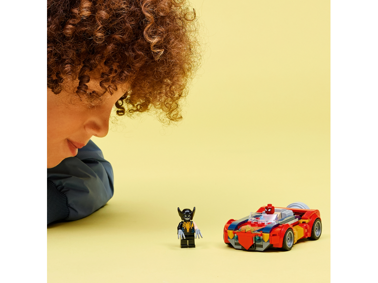 Ein Kind betrachtet eine Spielzeug-Superheldenfigur und ein rotes Spielzeugauto auf gelbem Grund.