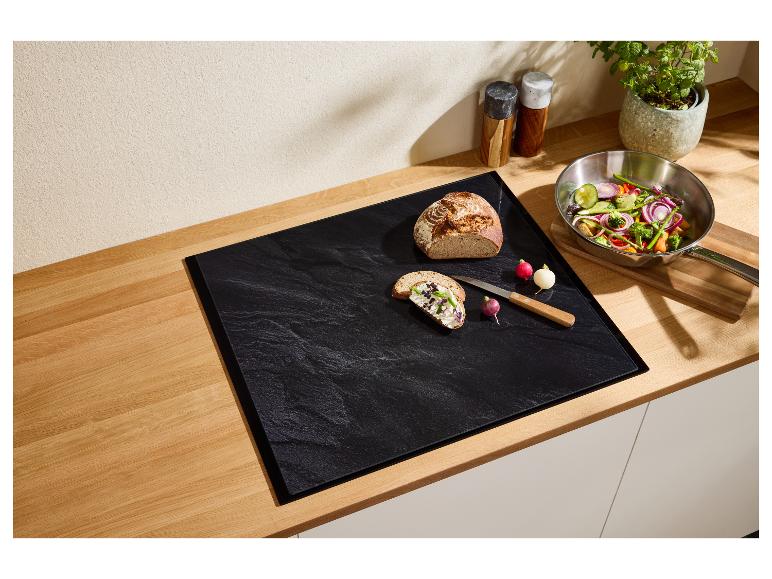 Küchenarbeitsplatte mit schwarzem Schneidebrett, Brot, Radieschen und einer Pfanne Gemüse.