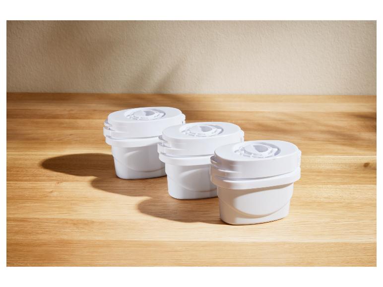 Drei weiße Wasserfilterkartuschen auf einem Holztisch.