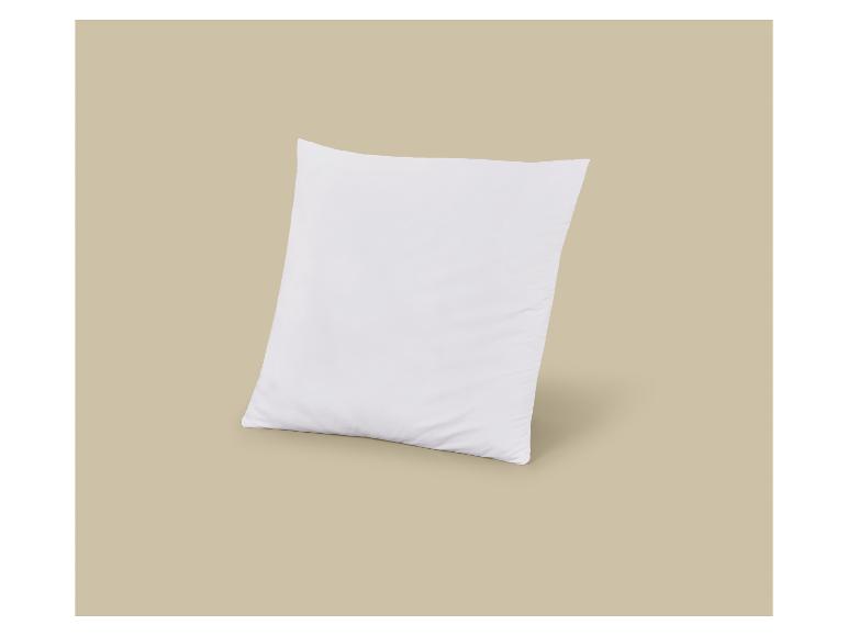 Ein weißes Kissen steht aufrecht auf einem hellbeigen Hintergrund.